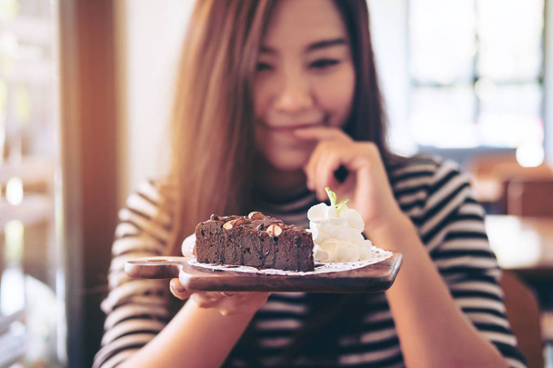 Krásná asijská žena držící brownie dort a šlehačkou s pocitem potěší a životní styl v moderní kavárně - Fotografie, Obrázek