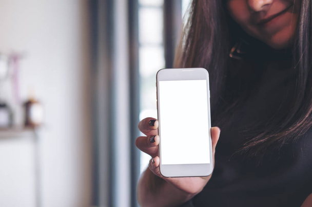 Изображение красивой женщины, держащей и показывающей белый мобильный телефон с чистым белым экраном и смайликом в современном кафе
 - Фото, изображение
