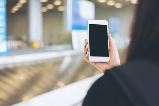 eine Frau, die ihr Handy in der Hand hält und benutzt, während sie auf die Gepäckausgabe am Flughafen wartet  - Foto, Bild