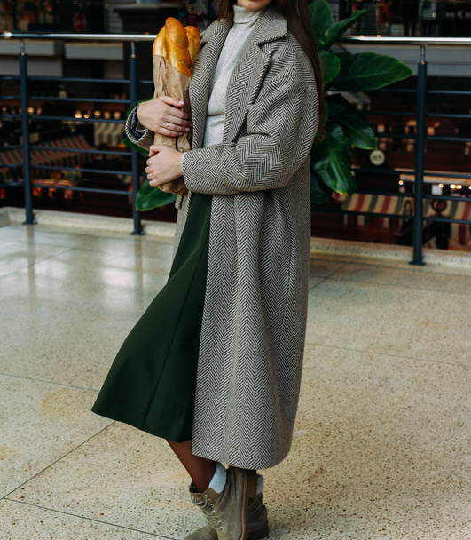 a girl in a coat is standing in a store with a baguette bag, breakfast, shopping,going to a grocery store.behind plants and market - Foto, Imagem