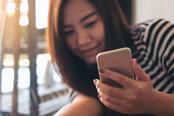Красивая азиатка, использующая смартфон с смайликом и чувствующая себя расслабленной в современном кафе
 - Фото, изображение