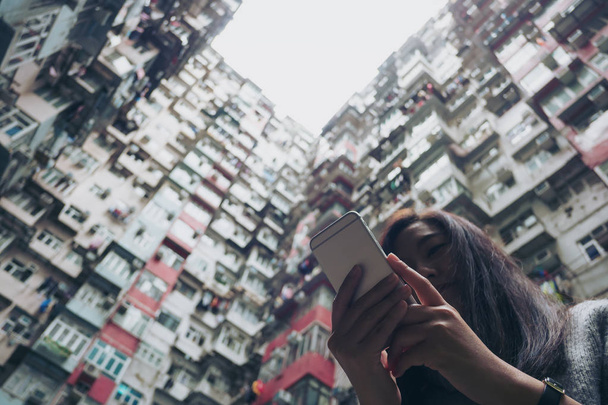 Siluety a nízký úhel obraz ženy pomocí mobilního telefonu s přeplněných bytového domu v komunitě v lomu Bay, Hong Kong pozadí  - Fotografie, Obrázek