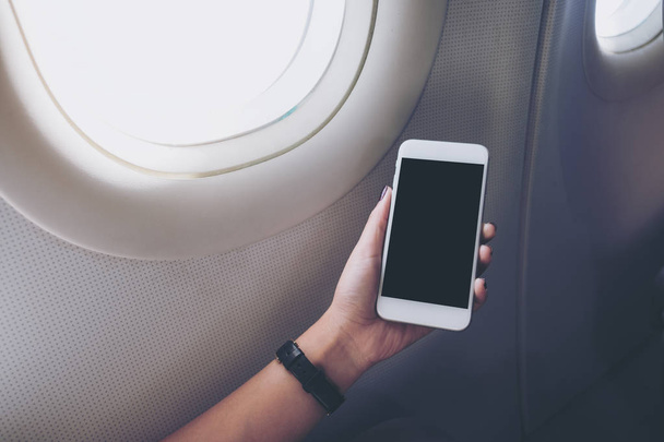 Egy kéz, gazdaság, és nézte a fehér szúró telefon fekete képernyő mellett a felhők és a háttérégbolt repülőgépen ablak makett képe - Fotó, kép
