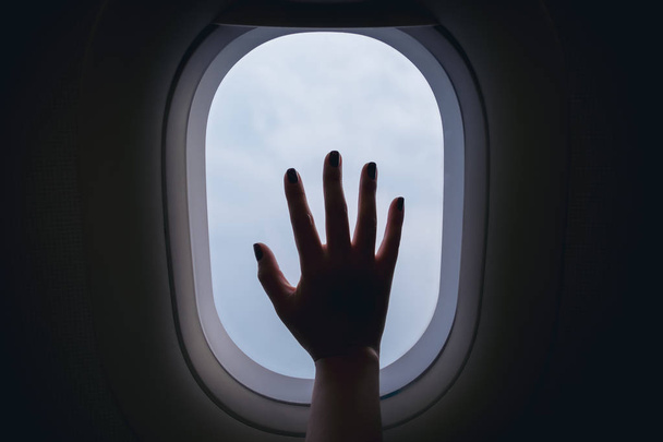 A woman's hand touching airplane window with clouds and sky background - Photo, Image