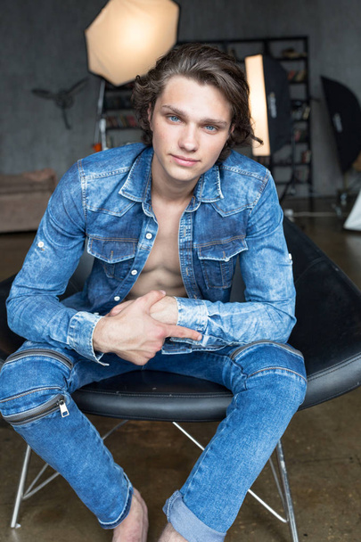 Handsome blond male model with blue eyes sitting in chair in blue denim - Photo, Image