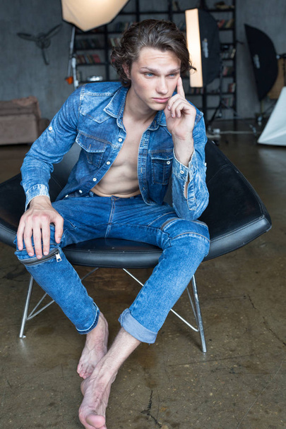 Handsome blond male model with blue eyes sitting in chair in blue denim - Foto, Imagem