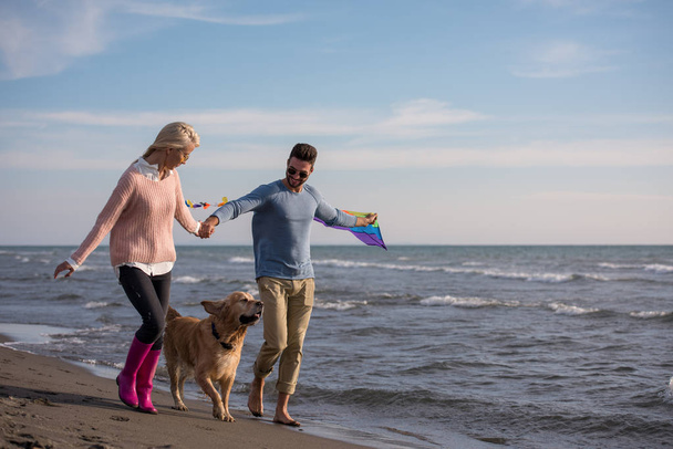 Young Couple having fun playing with a dog and Kite on the beach at autumn day - Fotoğraf, Görsel