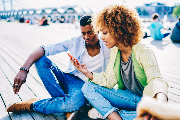 Afro-amerikai pár a szerelem segítségével korszerű smartphone, néz film online ül kint Városliget, nagyon sötét bőrű lány göndör haja megtekintés fénykép-Mobile részesedése a barátjával - Fotó, kép