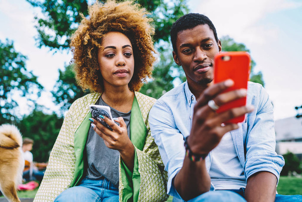 Handsome hipster guy sharing post with his girlfriend in networks using smartphone during date, afro american couple in love synchronizing multimedia files on cellulars having common photos - Fotoğraf, Görsel