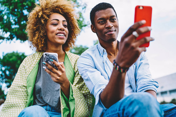 Couple in love having fun reading news and posts in social networks spending time on date in city park,dark-skinned friend choosing photo for update profile picture viewing images on smartphone - Photo, Image