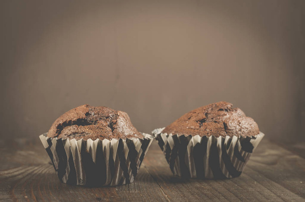 two chocolate muffins on a wooden table/two chocolate muffins on a wooden table. Dark style - Foto, Imagen