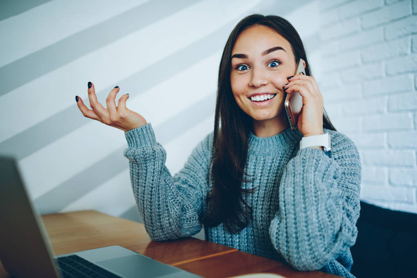 Half length portrait of happy young woman surprised about good news head during friendly phone conversation on smartphone sitting at computer in university.Positive student talking on cellular device - 写真・画像