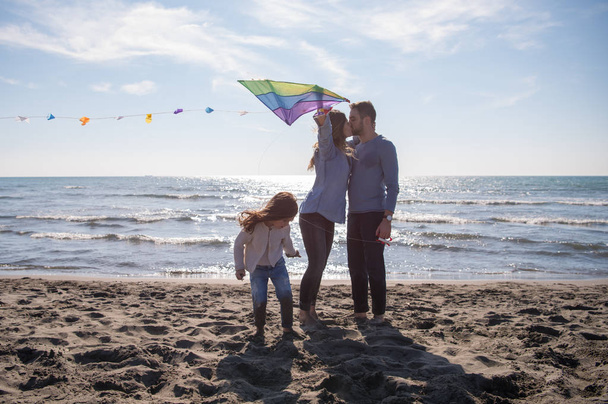 young family with kids resting and having fun with a kite at beach during autumn day - Photo, Image