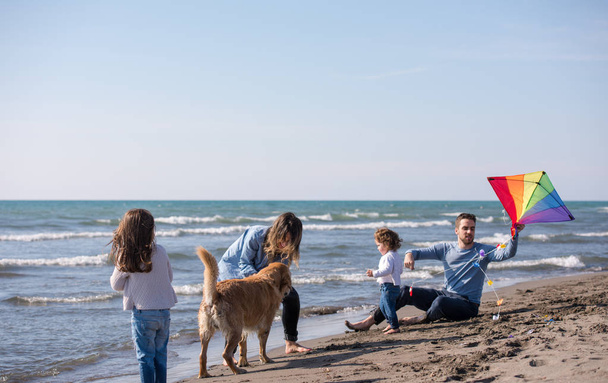 Mutlu ve çocuklu bir aile sonbahar günü sahilde köpek ve uçurtmayla eğleniyor. - Fotoğraf, Görsel