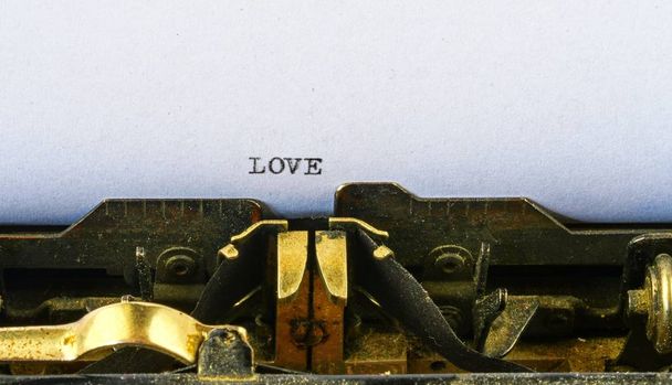 Κινηματογράφηση σε πρώτο πλάνο σε vintage γραφομηχανή. Εμπρός εστίαση σε επιστολές που κάνουν το κείμενο αγάπη. Ρομαντική έννοια εικόνα με ρετρό office εργαλείο. - Φωτογραφία, εικόνα