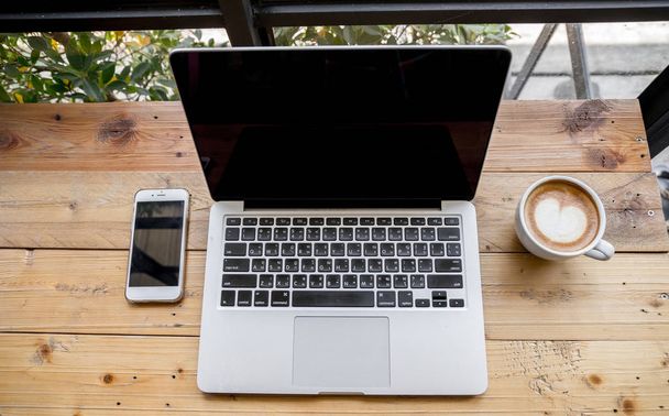 Vista superior del ordenador portátil con teléfono móvil y una taza de café fresco arte latte en la mesa de madera
. - Foto, Imagen