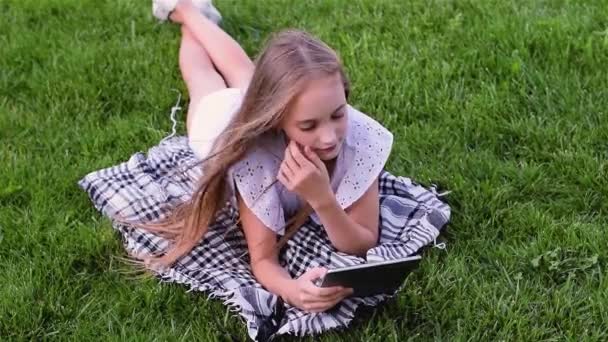 Menina feliz usando tablet pc encontra-se na grama no parque
 - Filmagem, Vídeo