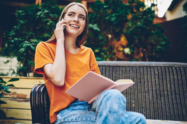 Uroczy czytnik kobiece rozmowy z operatorem komórkowym na nowoczesny telefon spędzać wolny czas na ulubioną książką siedzi w miejskie w pobliżu obszar reklamy reklama obszar - Zdjęcie, obraz