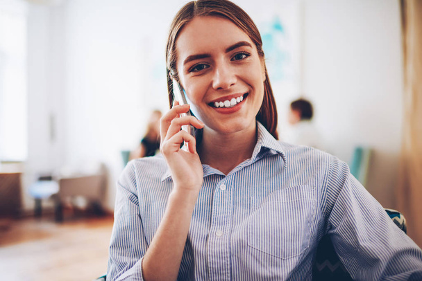 Half length portrait of cheerful blonde hipster girl smiling at camera while talking with operator on phone about confirmation of online order.Female manager having mobile conversation on cellular - Foto, Bild