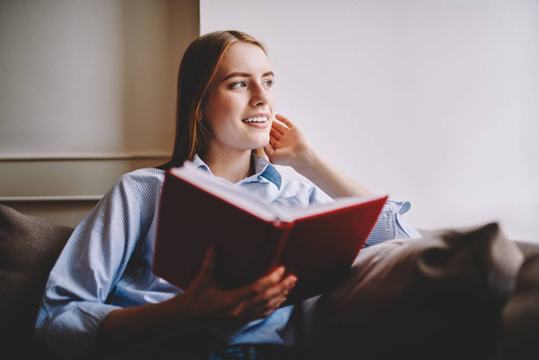 Thoughtful young woman analyzing novel after finishing reading text spending free time at home on weekends.Dreaming hipster girl thinking about continuation of love story of favorite book in coworking - Фото, изображение