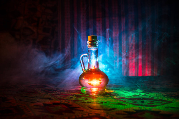 Antique and vintage glass bottle on dark foggy background with light. Poison or magic liquid concept. - Photo, Image