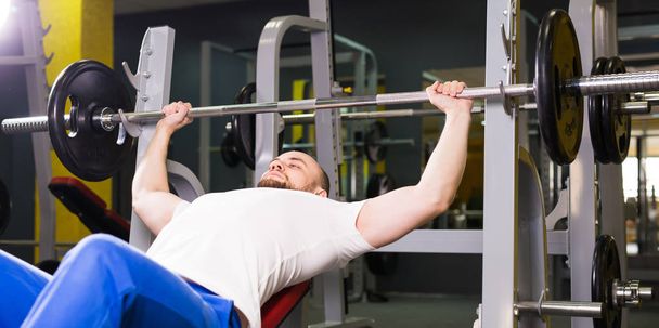 Sport, fitness, tréninku a lidé koncept - muž při bench pressu cvičení v tělocvičně - Fotografie, Obrázek