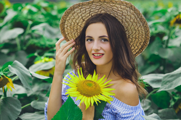 Young beautiful girl in dress and hat in field with sunflowers - Фото, зображення