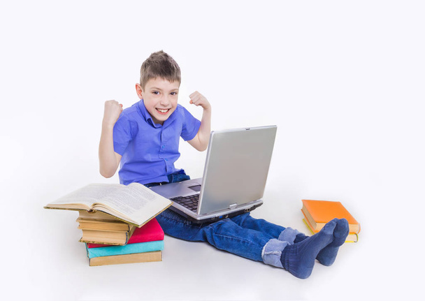 Portrait of cute schoolboy sitting with books and typing on laptop keyboard - Photo, Image