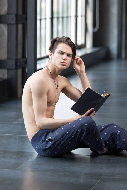 Handsome slim young guy shirtless in a pyjamas bottoms in a trendy dark room sitting on a floor - 写真・画像