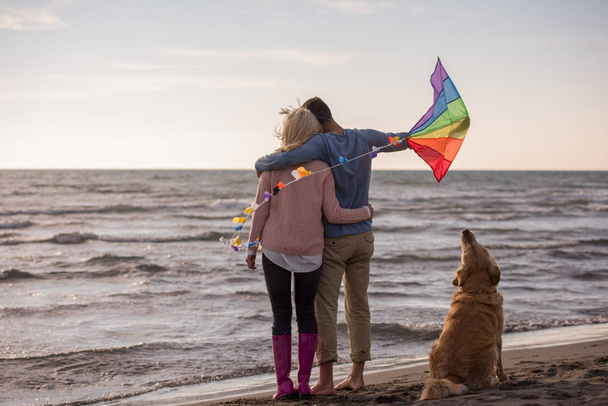 Young Couple having fun playing with a dog and Kite on the beach at autumn day - Фото, изображение