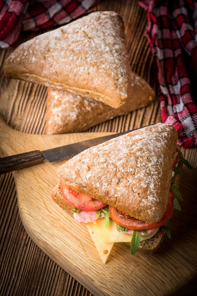 Triangular sandwich with cheese, ham and tomato on a wooden table. - Фото, зображення
