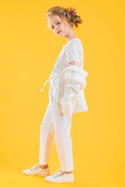A teenage girl in white clothes posing on a yellow background. The girl lowered her jacket to her elbows. - 写真・画像