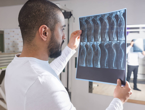 Close Up of Male Physiotherapist or Chiropractor or Doctor Looking at X-Ray Film of Spine in front of Light Box in Clinic - Fotografie, Obrázek