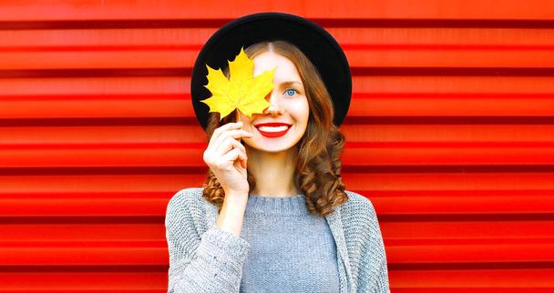 Happy cool girl  hides one eye yellow maple leaf on a red background - Foto, Imagen