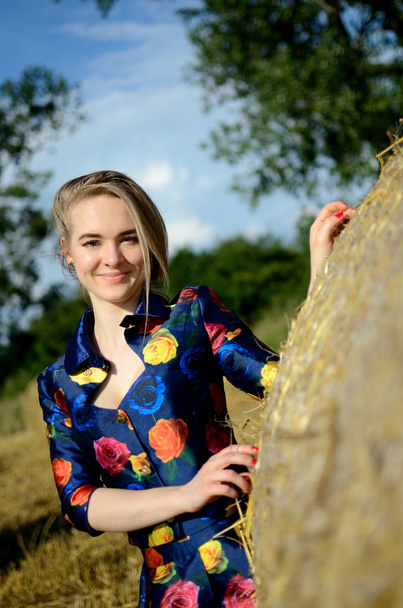 Nainen malli Ukrainasta poseeraa Puolan maatilalla. Nuori nainen yllään värikäs mekko seisoo vieressä heinää paali
. - Valokuva, kuva