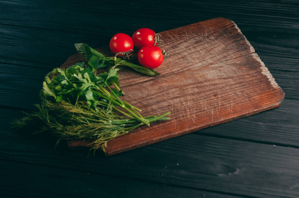Tomatoes, parsley and dill on a wooden cutting board on a black wooden background. View of the sperm, place under the text - Fotoğraf, Görsel