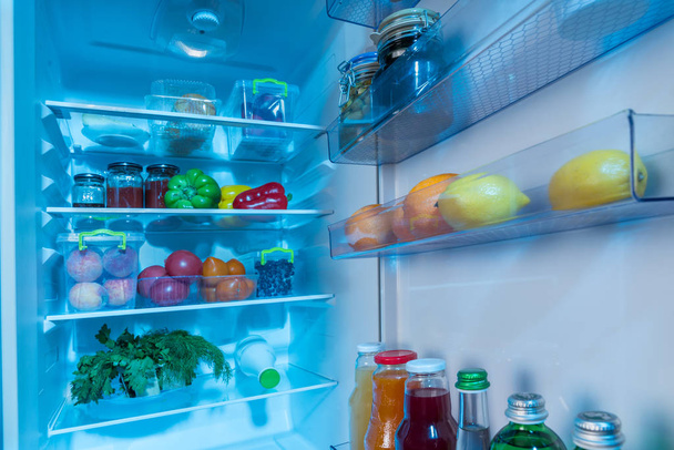 Open interior of a fridge packed with fresh vegetables, fruit and juice in a healthy diet concept - Zdjęcie, obraz