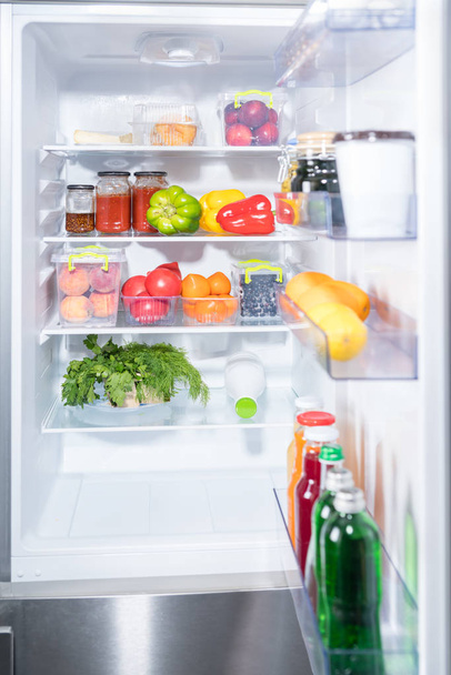 Open door of a fridge with fresh fruit and vegetables on the shelves and bottles of juice and beverage in the door - Foto, Bild