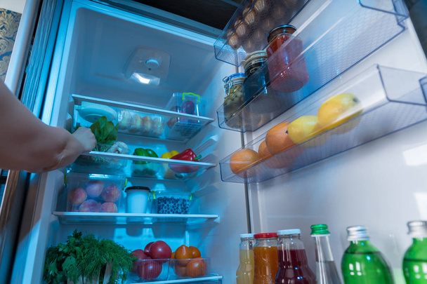 Person reaching for fresh vegetables in open refrigerator - Foto, Imagem