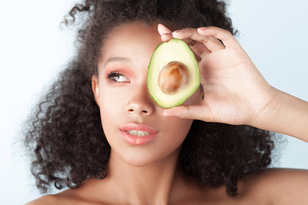 Young smiling black girl with clean perfect skin with avocado close-up. Beauty portrait - Fotografie, Obrázek