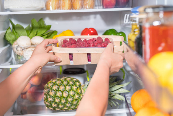 Person taking basket with fresh raspberries from open fridge - Photo, Image