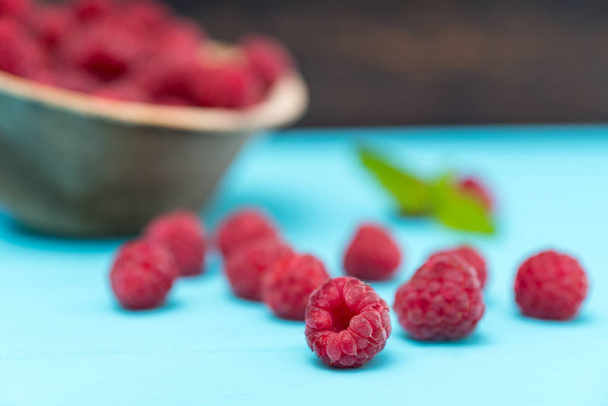 Freshly picked raspberries on blue table against bowl of fruits - Foto, Imagen
