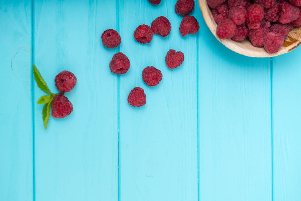 Plate of ripe raspberries with spilled fruit over a blue wooden background with copy space viewed from above - Foto, Imagen