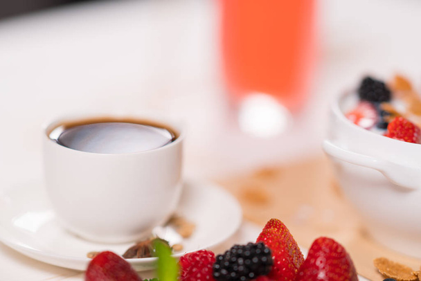 Cup of strong black espresso coffee for breakfast viewed past fresh berries with strawberry, raspberry, blackberry with lateral copy space - Foto, imagen