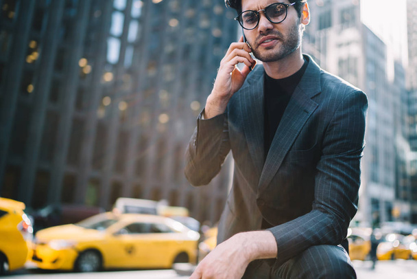 Image recadrée d'un trader confiant vêtu d'un costume élégant parlant avec un partenaire d'affaires sur un smartphone debout dans la rue Manhattan.
 - Photo, image