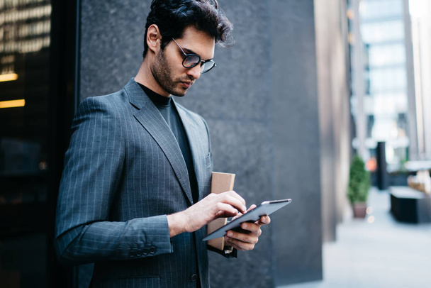 Pensive proud CEO in formal wear updating application with financial news on digital tablt connected to 4G internet on street.Confident businessman checking mail on touch pad near office building - Foto, imagen
