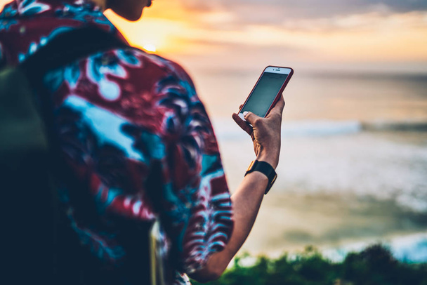 Back view of female traveler holding gadget and texting message for sending to friends while standing against ocean.Cropped image of hipster girl enjoying summer vacation with modern technology - Foto, imagen