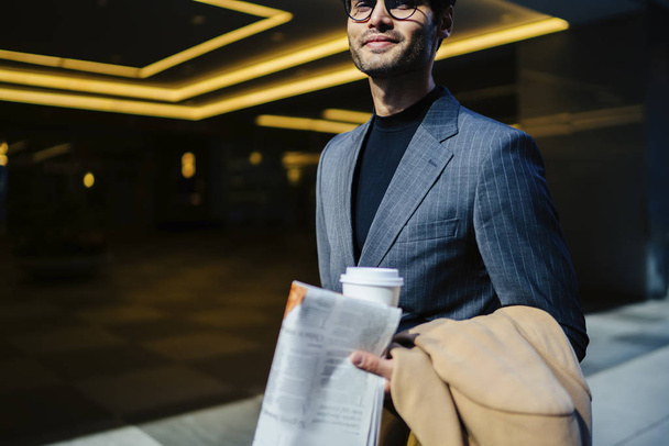 Cropped image of prosperous male in elegant suit walking with newspaper and coffee to go,positive business man dressed in trendy outfit satisfied with successful job carrying financial magazin - Valokuva, kuva