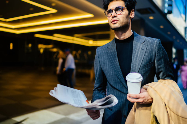 Confident trendy dressed male finance director thinking about article in daily newspaper walking with blank coffee to go cup, handsome proud ceo in elegant formal wear with press in hand in downtow - Foto, afbeelding