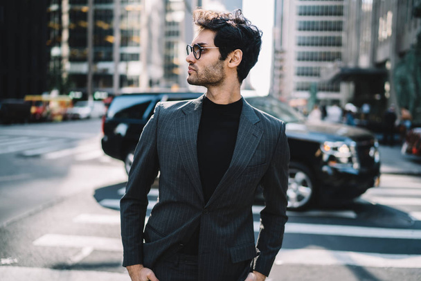 Side view of handsome proud male ceo in fashion formal wear standing on luxury car background on Manhattan, confident businessman in elegant suit looking away spending time on avenue urban setting - Foto, Bild